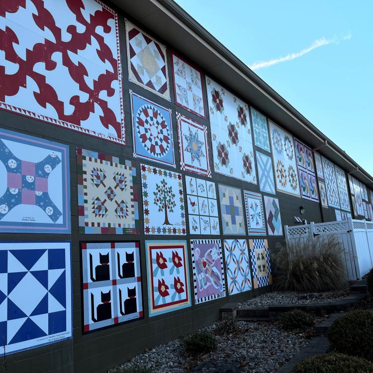  metal quilt signs on the side of a building, white small fence